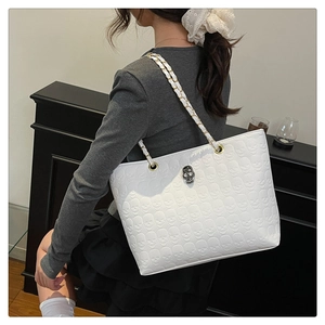Detail of white skull embossed tote with metal skull buckle and chain strap on shoulder