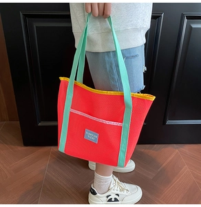 Detail of red mesh tote bag with green handles and yellow trim for beach and gym gear