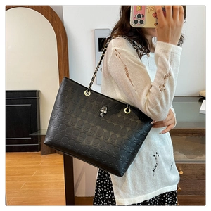 Detail of black tote bag with embossed skull patterns and rhinestone metal skull charm