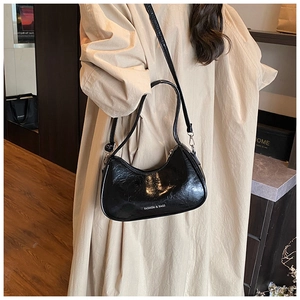 Close-up of black glossy crescent hobo bag with Fashion & Bags text on beige coat