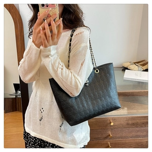 Detail of black leather tote bag featuring embossed skull pattern and gold chain strap