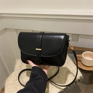 Borsa a tracolla nera minimalista con dettagli dorati su una coperta beige