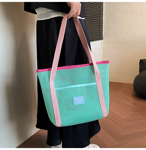 Detail of mint green mesh beach bag with pink straps shown held by a model