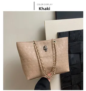 Detail of khaki tote bag featuring embossed skull texture and metal chain strap