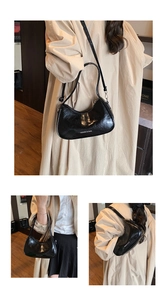 Detail of black wrinkled patent leather texture and white logo on hobo shoulder bag