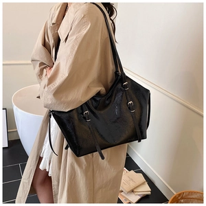 Chic black patent leather tote bag detail with decorative buckle straps on beige coat
