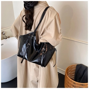 Detail view of glossy black faux leather tote bag featuring elegant silver side buckles