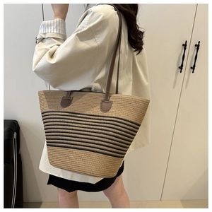 Détail d'un sac cabas en paille tissé avec rayures noires et anses en cuir marron