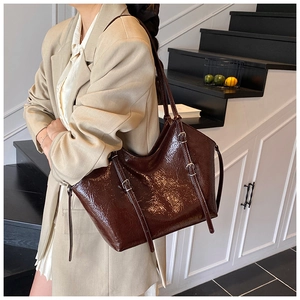 Close-up of large dark brown tote bag with glossy patent leather and buckle details