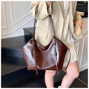 Detail of dark brown leather tote bag with glossy finish and decorative metal buckles
