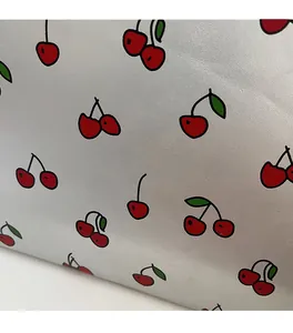 Close-up of silver textured leather fabric with vibrant red cherry patterns and green leaves