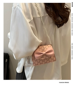 Close-up of pink mini crossbody bag with M-pattern leather, bow, and pearl strap