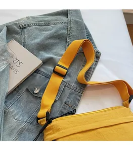 Dettaglio borsa a tracolla in nylon giallo con ampia tracolla su sfondo di giacca denim