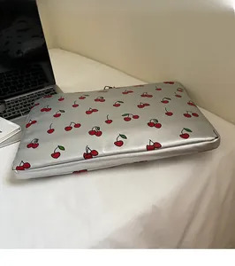Silver laptop sleeve with red cherry pattern on desk next to a laptop computer