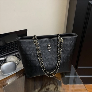 Retro black tote bag with embossed skull patterns and metal chain straps on a desk