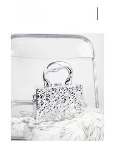 Detail shot of silver acrylic evening bag with lava texture and metal handle on white plush