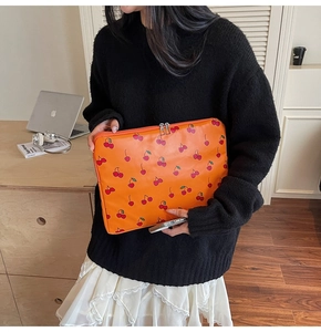 Detail of orange cherry print laptop sleeve with zipper closure held by a person