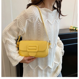 Detail of a bright yellow leather shoulder bag with square buckle worn by a model