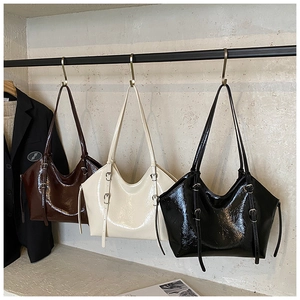 Three patent leather tote bags in black, cream, and brown hanging on a metal display rack