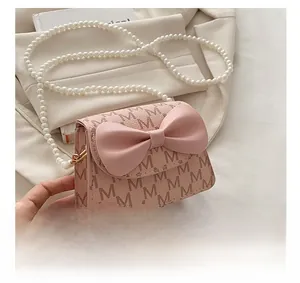 Detail of light pink mini bag with embossed M pattern, leather bow, and pearl chain