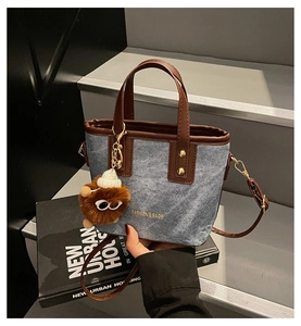Detail view of denim tote bag with leather trim, gold studs and fuzzy monster charm