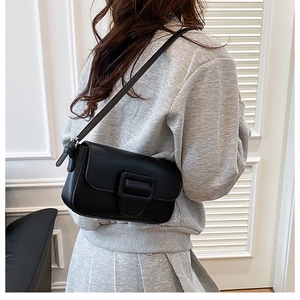 Side view of a black leather shoulder bag with a large square buckle on a female model