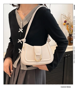 Detail of cream leather shoulder bag with gold metal hardware and knotted strap on model