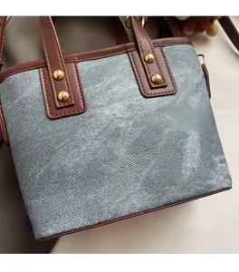 Detail of denim and brown leather bucket bag with gold rivets and fashion lettering