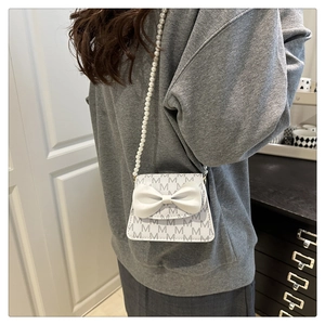 Detail of white leather mini bag featuring M-pattern, 3D bow and pearl bead strap