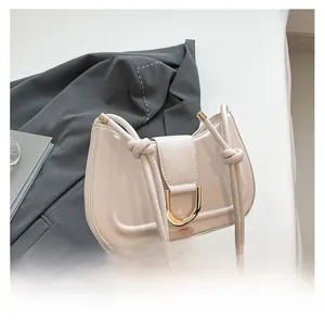 Detail of a creamy white saddle bag with a large gold U-shaped metal buckle and knot strap