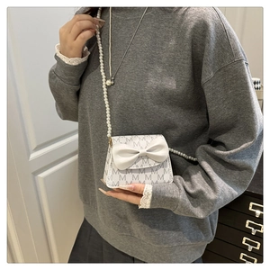 Close-up of girls mini pearl strap handbag with elegant bow and grey monogram pattern