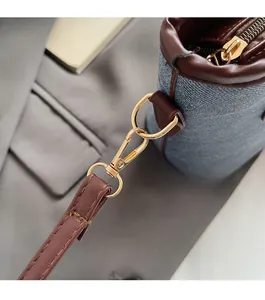 Close-up of golden hardware, brown leather strap, and blue denim texture on bucket bag