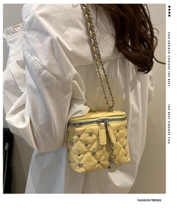Close-up view of the yellow quilted box bag featuring metal studs and chain strap