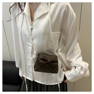 Detail of a brown mini crossbody bag with M-pattern print and large bow decoration