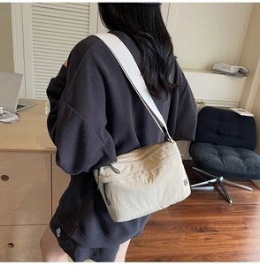 Dettaglio di una borsa a tracolla in nylon beige con ampia tracolla grigia indossata