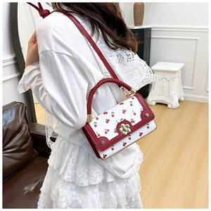 Close-up of a white and red cherry print crossbody bag with a gold flower lock detail