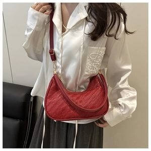 Détail du sac hobo en cuir tressé rouge avec boucle dorée sur fond de chemise en soie