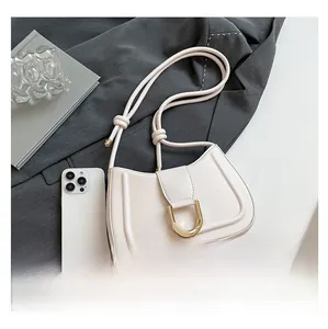 White leather shoulder bag with gold U-shaped buckle and dual straps beside a smartphone