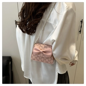 Detail of pink bow handbag with M-pattern print and elegant pearl chain strap