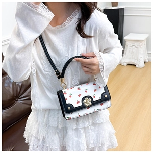 Close-up of cherry print crossbody bag with flower clasp and woven handle detail