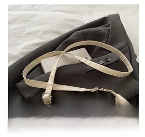 Close-up of cream PU leather shoulder strap with silver buckle on a gray blazer