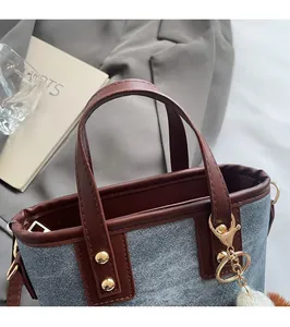 Detail of blue denim bucket bag featuring brown leather trim and gold metal rivets