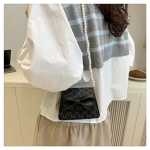 Detail of a black mini crossbody bag featuring a leather bow and white pearl shoulder strap