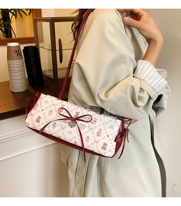 Detail of white quilted underarm bag with cartoon print and large red bow accent