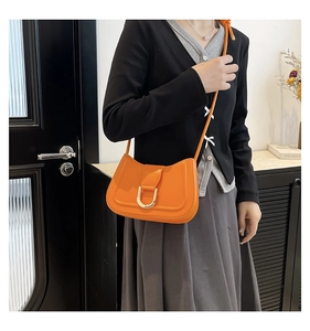 Close-up of orange leather crossbody bag with U-shaped gold buckle worn by a model
