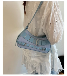 Detail view of light blue denim saddle bag with metal eyelets and adjustable strap