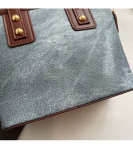 Close-up of blue denim bucket bag with brown leather accents and gold rivet details