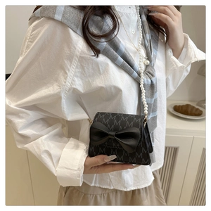 Detail of mini black crossbody bag with large bow, pearl strap and M-letter pattern