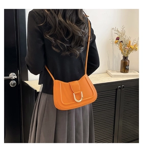 Detail of bright orange saddle bag with gold U-shaped buckle in a lifestyle setting