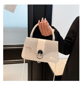Detail einer eleganten cremefarbenen Handtasche mit glitzernder Klappe und Verschluss